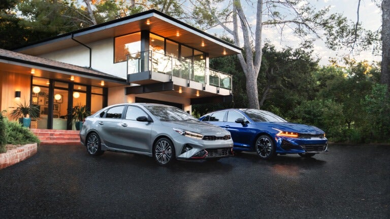 Kia K5 and Kia Forte sedans parked in front of a modern city backdrop